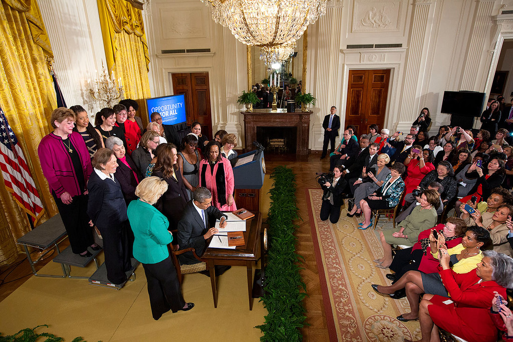 President Barack Obama signs executive actions to strengthen enforcement of equal pay laws for women, at an event marking Equal Pay Day in the East Room of the White House, April 8, 2014. The President signs the Presidential Memorandum -- Advancing Pay Equality Through Compensation Data Collection, and an Executive Order regarding Non-Retaliation for Disclosure of Compensation Information. Lilly Ledbetter stands to the left of the signing table. (Official White House Photo by Chuck Kennedy)