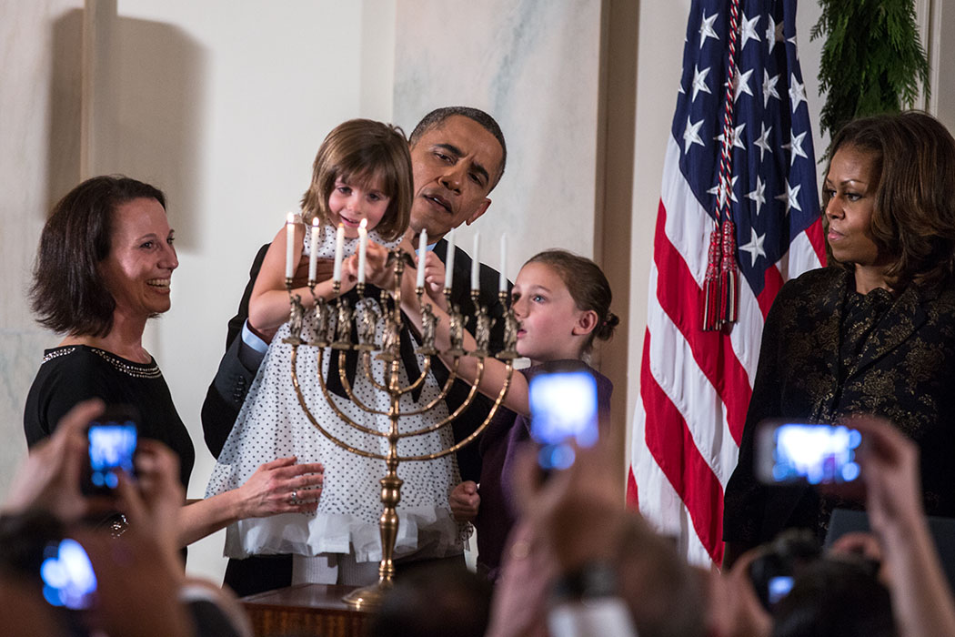 President Barack Obama holds up Kylie Schmitter as she and her sister Lainey Schmitter light the menorah during the Hanukkah reception in the Grand Foyer of the White House, Dec. 5, 2013. (Official White House Photo by Lawrence Jackson)