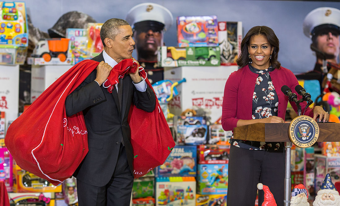 First Lady Michelle Obama, with President Obama carrying bags of toys, speaks at Toys for Tots event