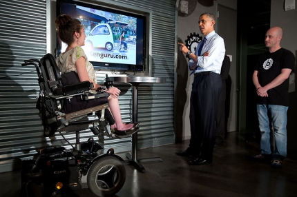 President Barack Obama listens to a presentation about a new car that you can drive a wheelchair into
