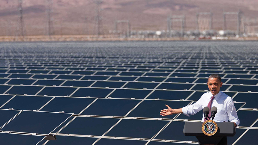 President Obama speaks about clean energy with a field of solar panels behind him.